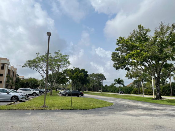 View of a parking area with trees and a building in the background.