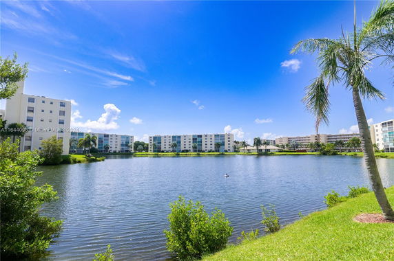 View of apartment buildings across a lake with palm trees in the foreground.