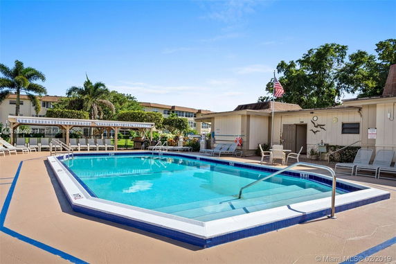 Outdoor swimming pool with surrounding deck chairs and a small building nearby.