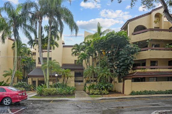 Front view of a multi-story residential building with balconies and surrounding palm trees.