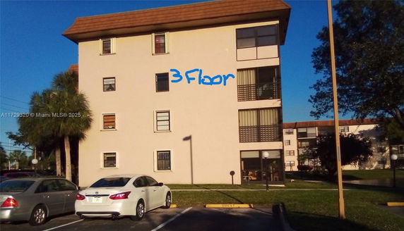 Front view of a multi-story residential building with marked third floor and parking area.