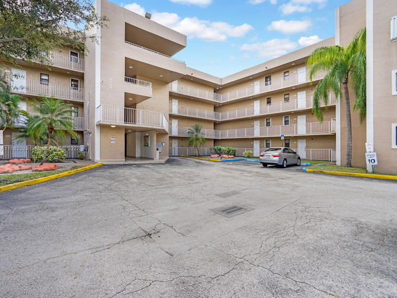 Front view of a multi-story residential building with balconies and a parking area.