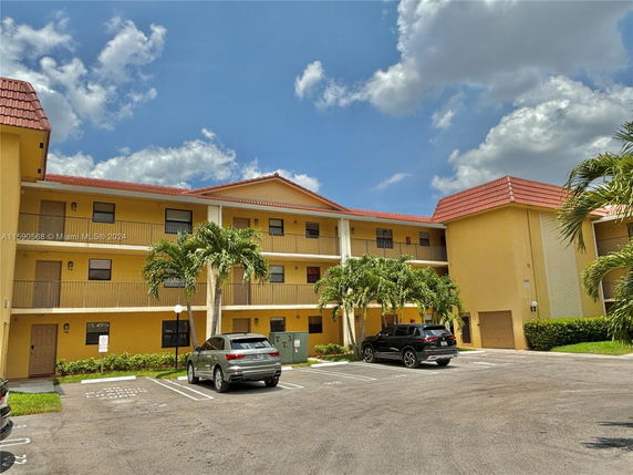 Front view of a multi-story apartment building with red-tiled roofs and parking area.