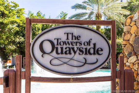 Sign for 'The Towers of Quayside' with trees and a stone wall in the background.