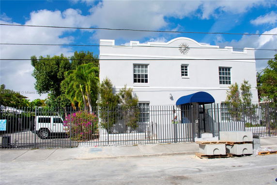 Front view of a two-story white building with a blue awning and gated entrance.