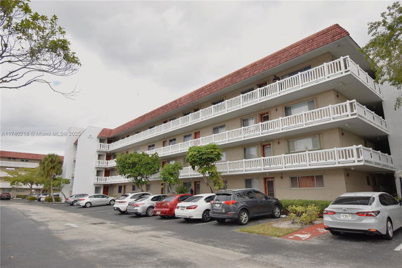 Front view of a multi-story apartment building with balconies and a parking area in front.