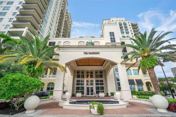 Front view of a multi-story building with an arched entrance and palm trees.