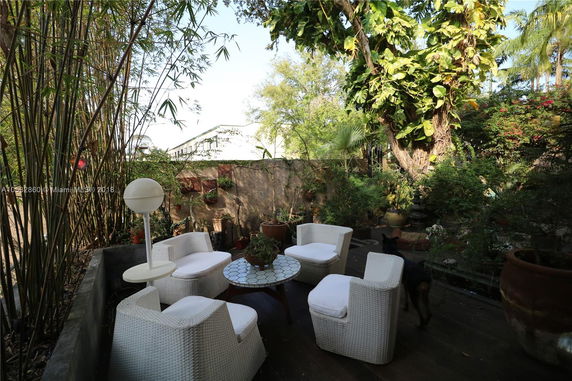 Outdoor seating area with wicker chairs and a round table surrounded by lush greenery and a wooden deck.
