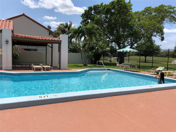 Outdoor swimming pool with lounge chairs and a shaded seating area.