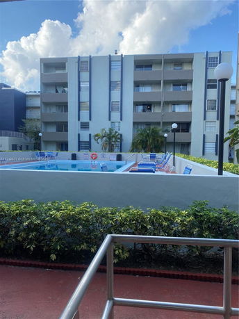 View of a multi-story residential building with balconies and a pool area in front.