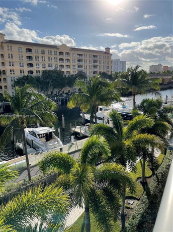 View of a multi-story building next to a waterway with yachts and palm trees.