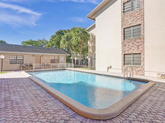 Outdoor swimming pool located next to a building with brick and stucco exterior.