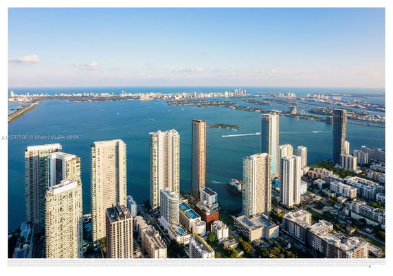 Aerial view of tall residential and commercial buildings by a body of water with a cityscape in the background.