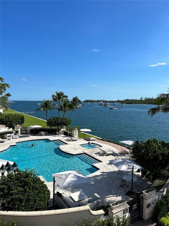 View of a swimming pool area overlooking a body of water with several boats and distant shoreline.
