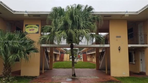 Front view of a two-story condo building with palm trees and external staircases.