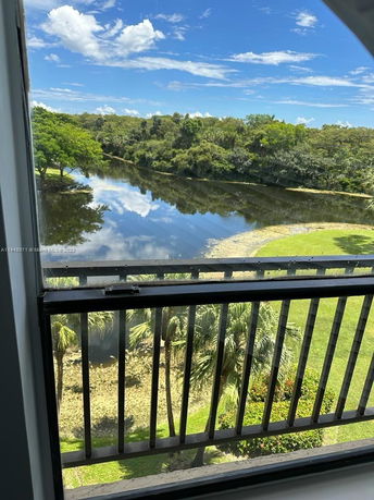 View from a window showing a landscape with a river, trees, and blue sky.