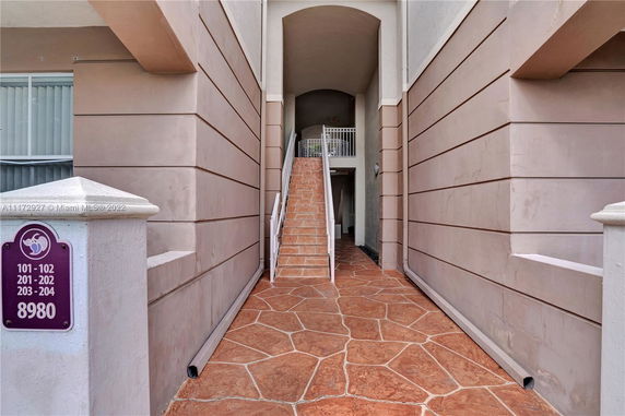 Exterior view of a building entrance with a walkway and stairs leading to an upper level.