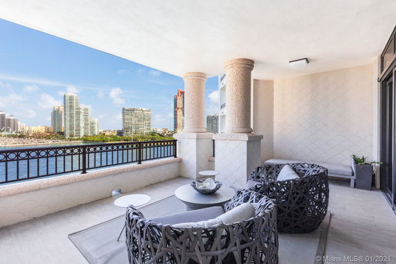 Balcony with woven chairs offering a view of tall modern buildings across a body of water.
