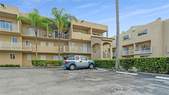 Front view of a multi-story apartment building with balconies and a parking area.