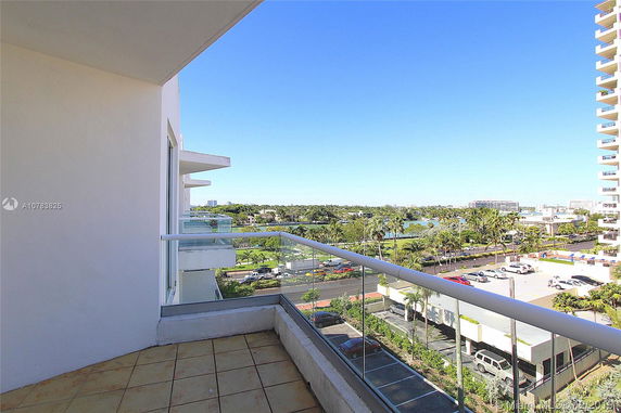 View from a balcony overlooking a parking area and distant greenery.