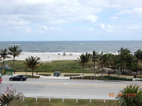View of the ocean and beach with palm trees from a roadside perspective.