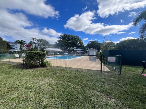 Outdoor swimming pool with surrounding greenery and a nearby building.