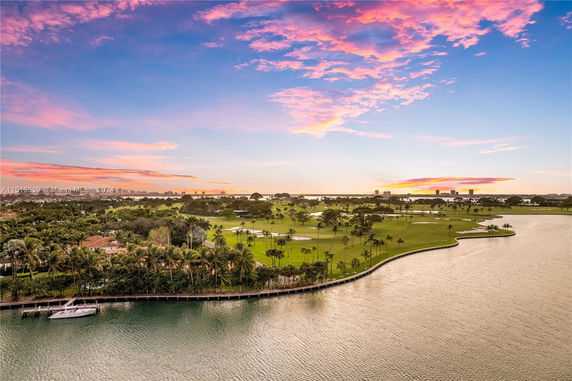 Scenic view of a waterfront area with a golf course and lush greenery under a colorful sunset sky.