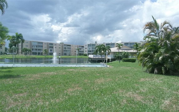 View of a residential building complex with a pond and fountain in front.