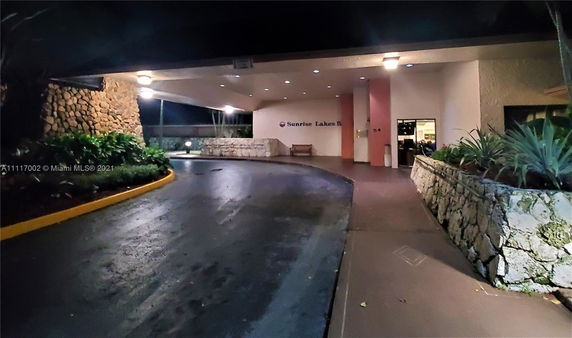 Exterior view of a building entrance with a covered driveway and stone walls.