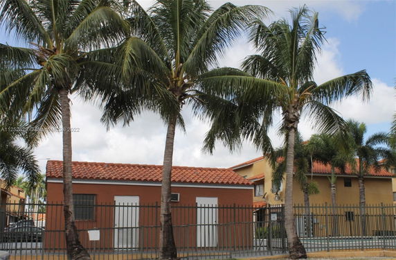 Front view of a house with red-tiled roofing and palm trees in front.