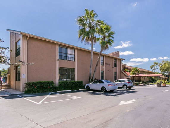 Front view of a two-story building with adjacent parking area and palm trees.