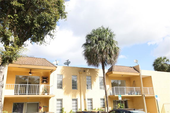 Front view of a two-story yellow building with balconies and satellite dishes.