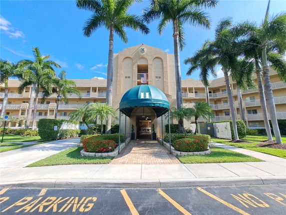 Front view of a multi-story residential building with palm trees and a covered entrance.