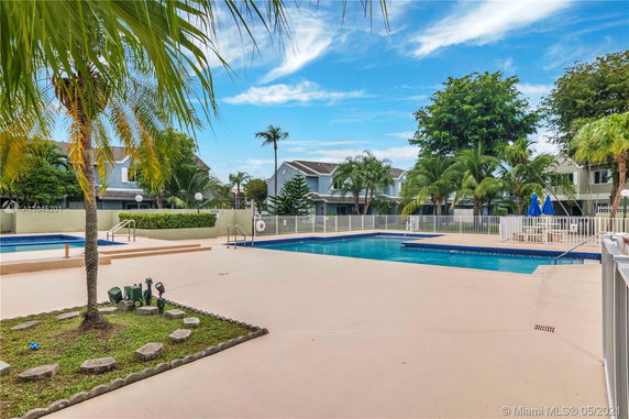 Outdoor swimming pool area with surrounding palm trees and residential buildings.