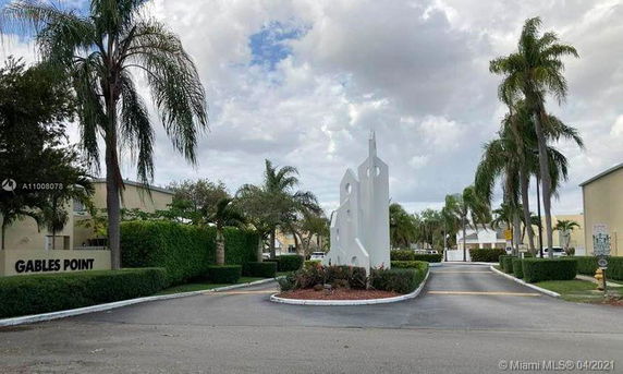 Entrance view of a residential complex with palm trees and a central sculpture.