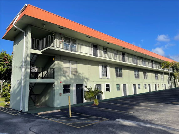 Front view of a three-story apartment building with a red roof and exterior stairs.