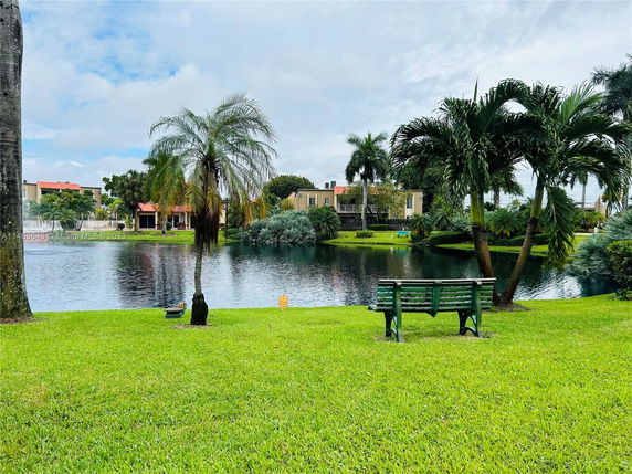 View of a serene lake with nearby residential buildings and palm trees.