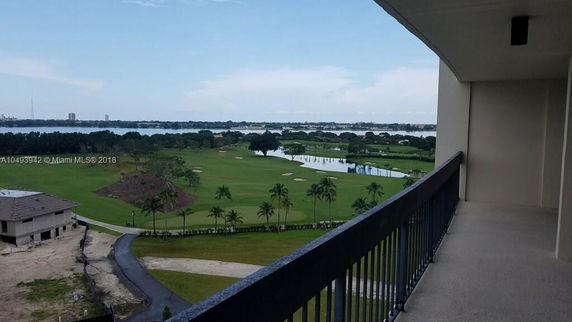 Panoramic view from a high-rise building showing a landscape with a golf course and a body of water in the distance.
