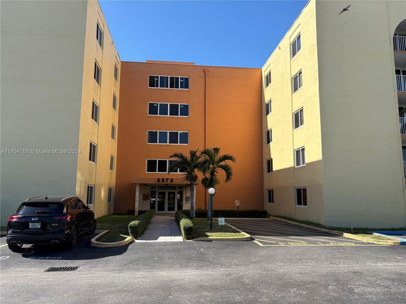 Front view of a multi-story apartment building with an entrance and adjacent parking area.