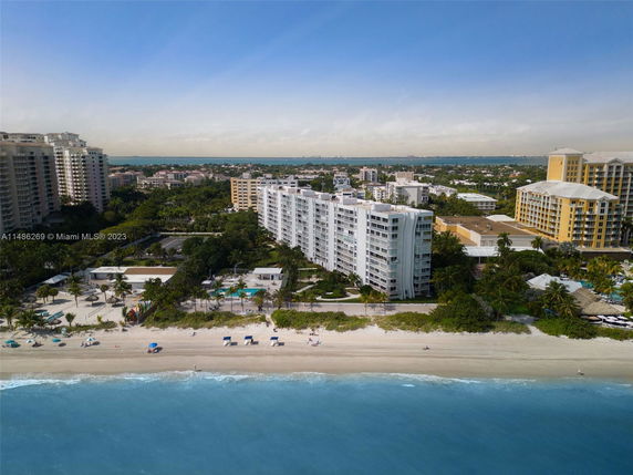 Aerial view of a beachfront high-rise building with surrounding structures and a beach.