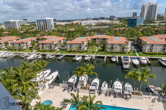 Aerial view of a residential area with condos, boats docked along a canal, and distant skyscrapers.