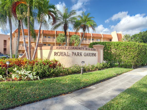 Front view of a multi-story adult community building with a decorative sign and palm trees.