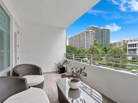 View from a balcony with outdoor seating, overlooking nearby buildings and greenery.