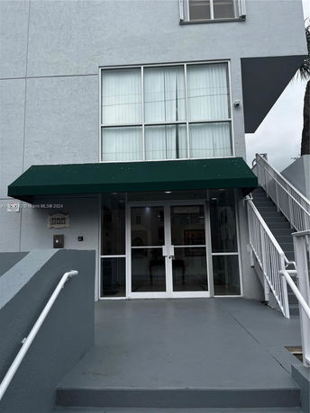 Entrance of a multi-story building with a green awning and glass double doors.