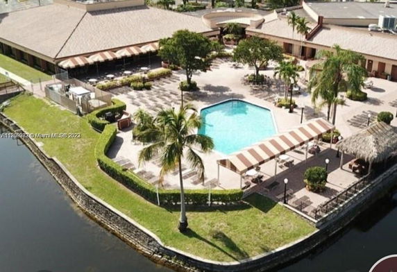 Outdoor view of a building complex with a central swimming pool area surrounded by palm trees and shaded seating.