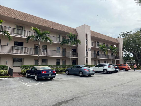 Front view of a three-story residential building with balconies and parked cars.