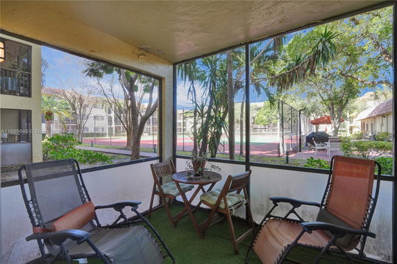 Outdoor seating area overlooking a fenced tennis court and surrounding greenery.