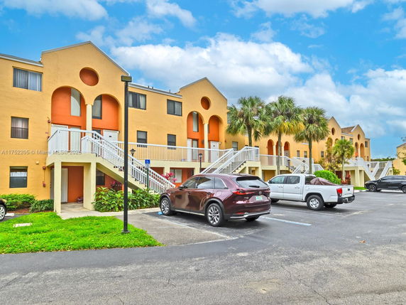 Front view of a multi-story apartment building with exterior staircases and parking area.