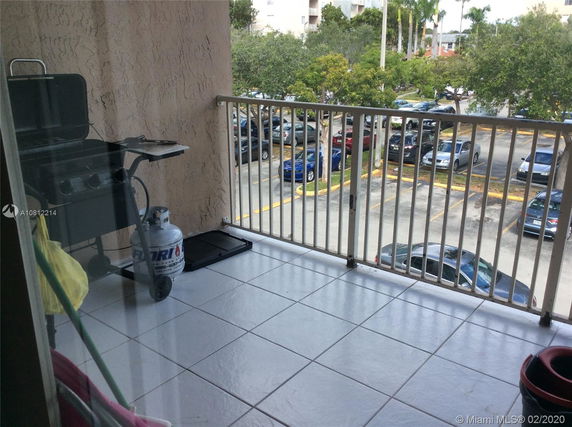 Balcony view overlooking a parking area with multiple parked cars and trees in the background.