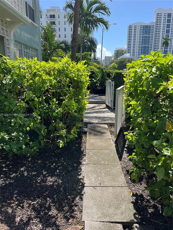 Pathway leading through lush greenery with buildings visible in the background.